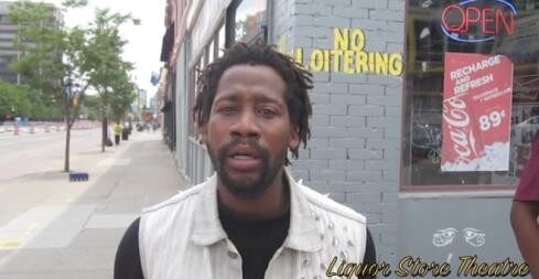 A man with short dreadlocks stands on a sidewalk in front of a store with signs that read "NO LOITERING" and "OPEN." There's also an advertisement for a beverage priced at 89 cents. The text "Liquor Store Theatre" is overlaid at the bottom of the image.