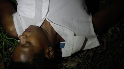 A person wearing a white shirt lies on the grass with eyes closed at night.