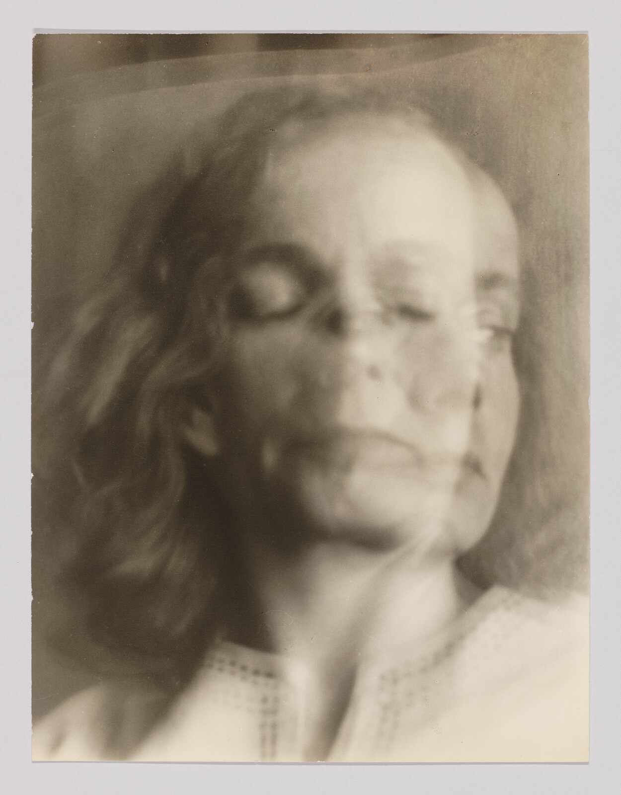 An older woman’s double-exposed portrait with eyes closed and a faint second profile overlapping.