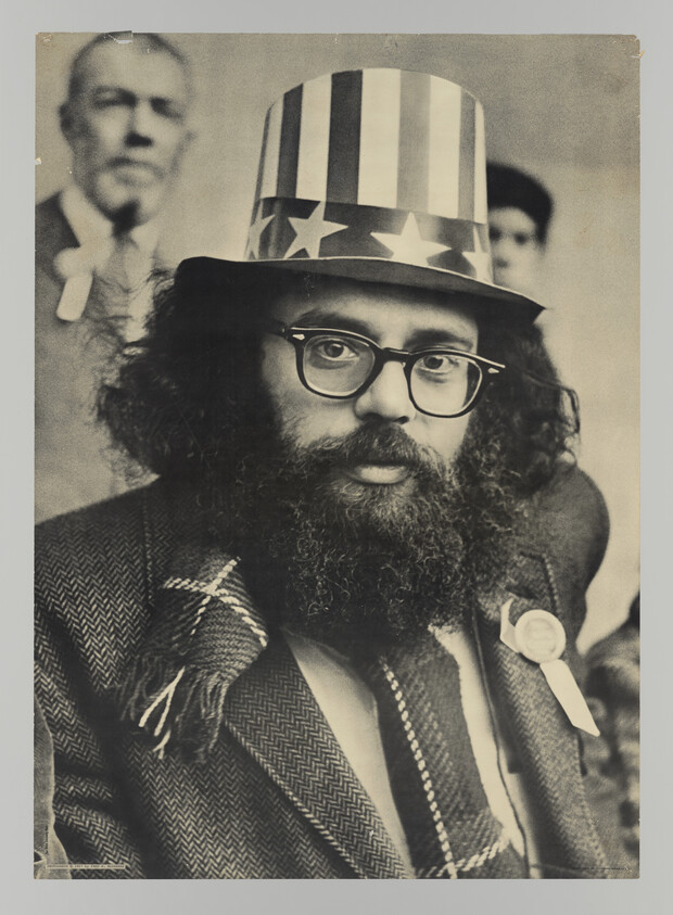 Bearded man with glasses wearing a stars-and-stripes top hat, scarf, and a ribbon pin.