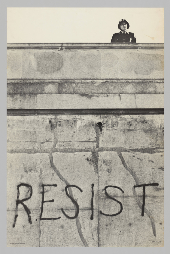 A black and white photograph showing a uniformed officer standing atop a high wall, looking down. Below the officer, the word "RESIST" is prominently graffitied on the wall in large, dark letters. The image conveys a sense of authority contrasted with a call to defiance.