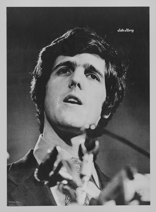 Young man speaking into multiple microphones with serious expression, viewed from low angle.