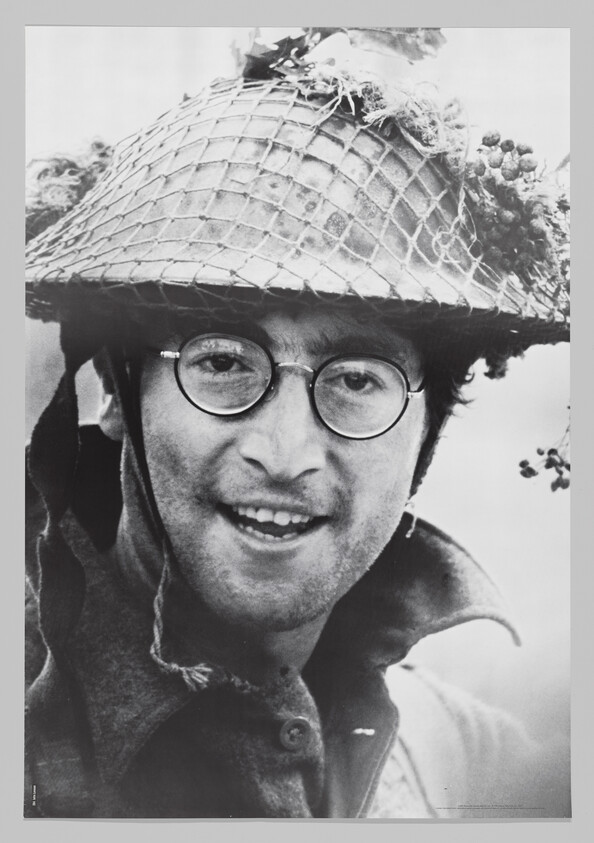Smiling man wearing round glasses and a netted military helmet looking toward the camera.