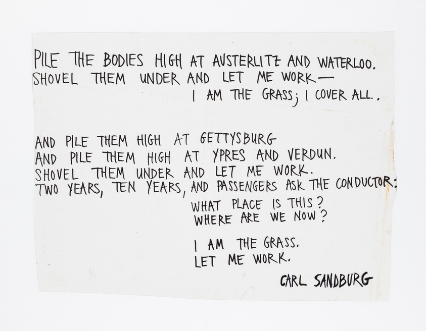 Handwritten poem excerpt by Carl Sandburg titled "I am the grass" written in black marker on paper.