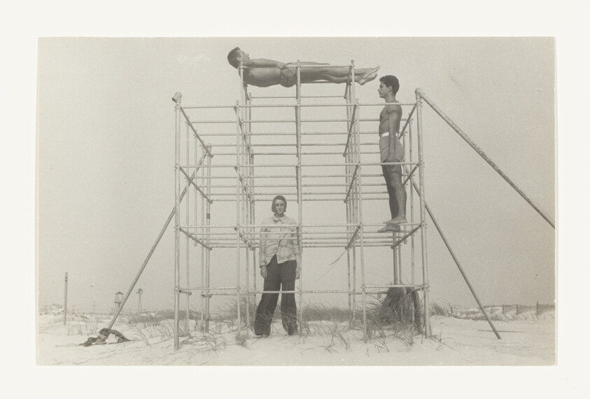 Three people on a metal structure at the beach, one lying on top, two standing below.