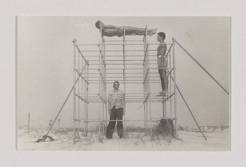 Three people on a metal structure at the beach, one lying on top, two standing below.