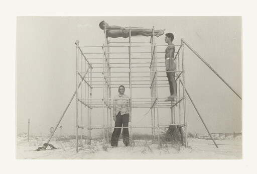 Three people on a metal structure at the beach, one lying on top, two standing below.