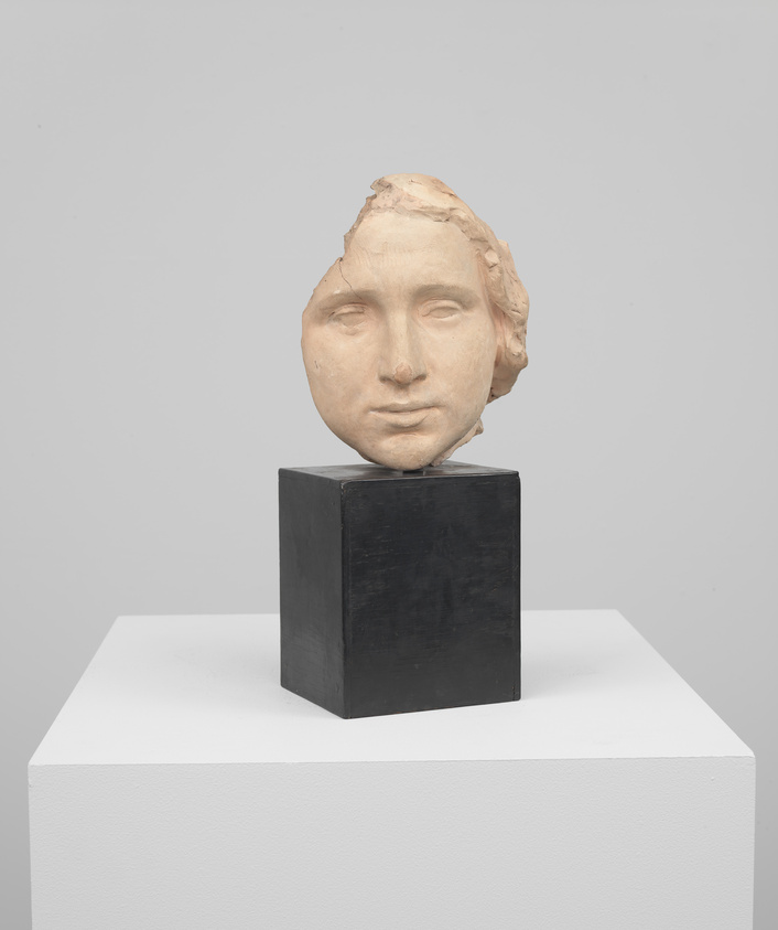 Sculpture of a fragmented human face on a black pedestal, displayed against a grey background.