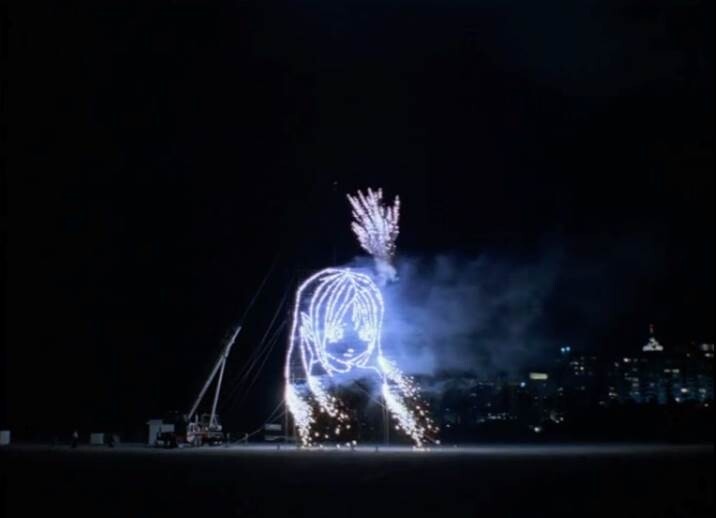 A large firework display forms a glowing outline of a girl's face with sparks falling.