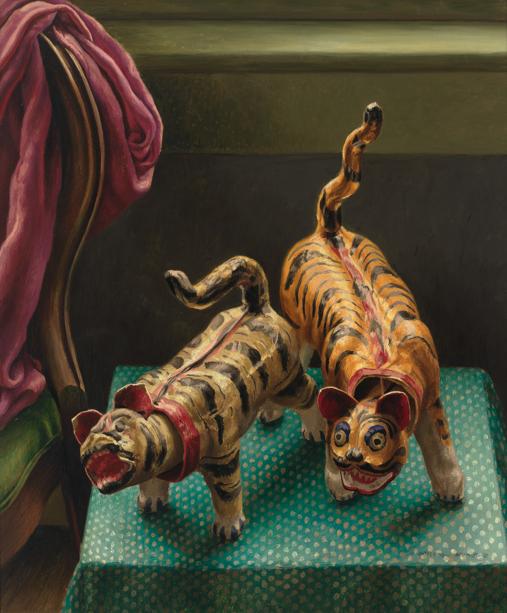 Two painted toy tigers stand on a green patterned table beside a chair draped with pink cloth.