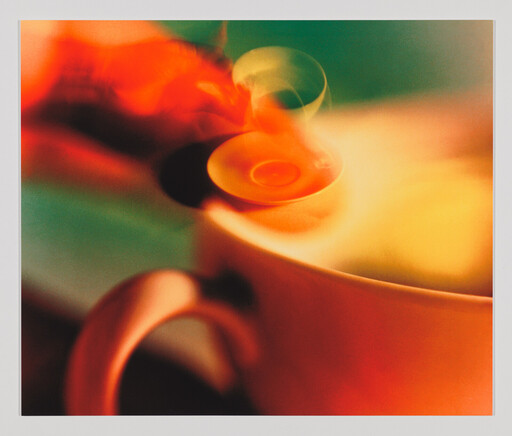 A steaming orange cup with a small spoon stirring and wisps of steam rising above.