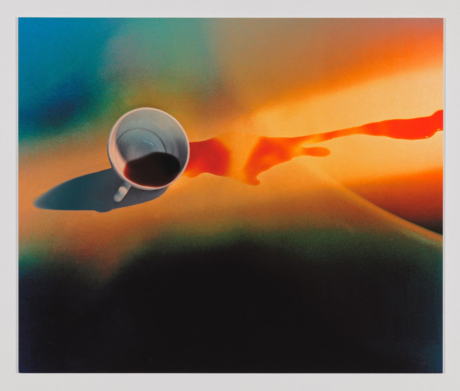 A white coffee cup with dark liquid casts a shadow across a colorful orange and blue surface.