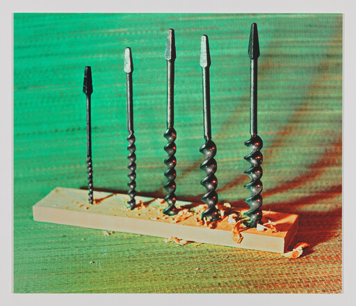 Six auger drill bits of increasing size standing upright in a wood block with shavings.