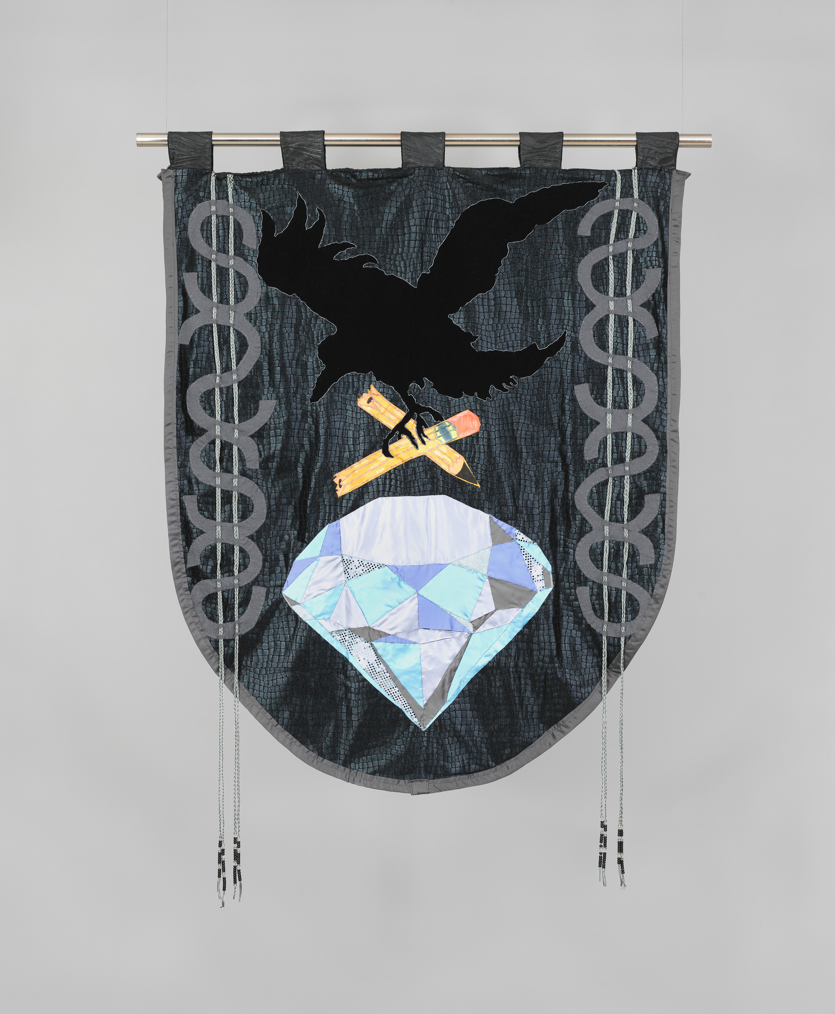 A black bird grasps two halves of a broken yellow pencil above a large diamond on a dark grey quilted banner.