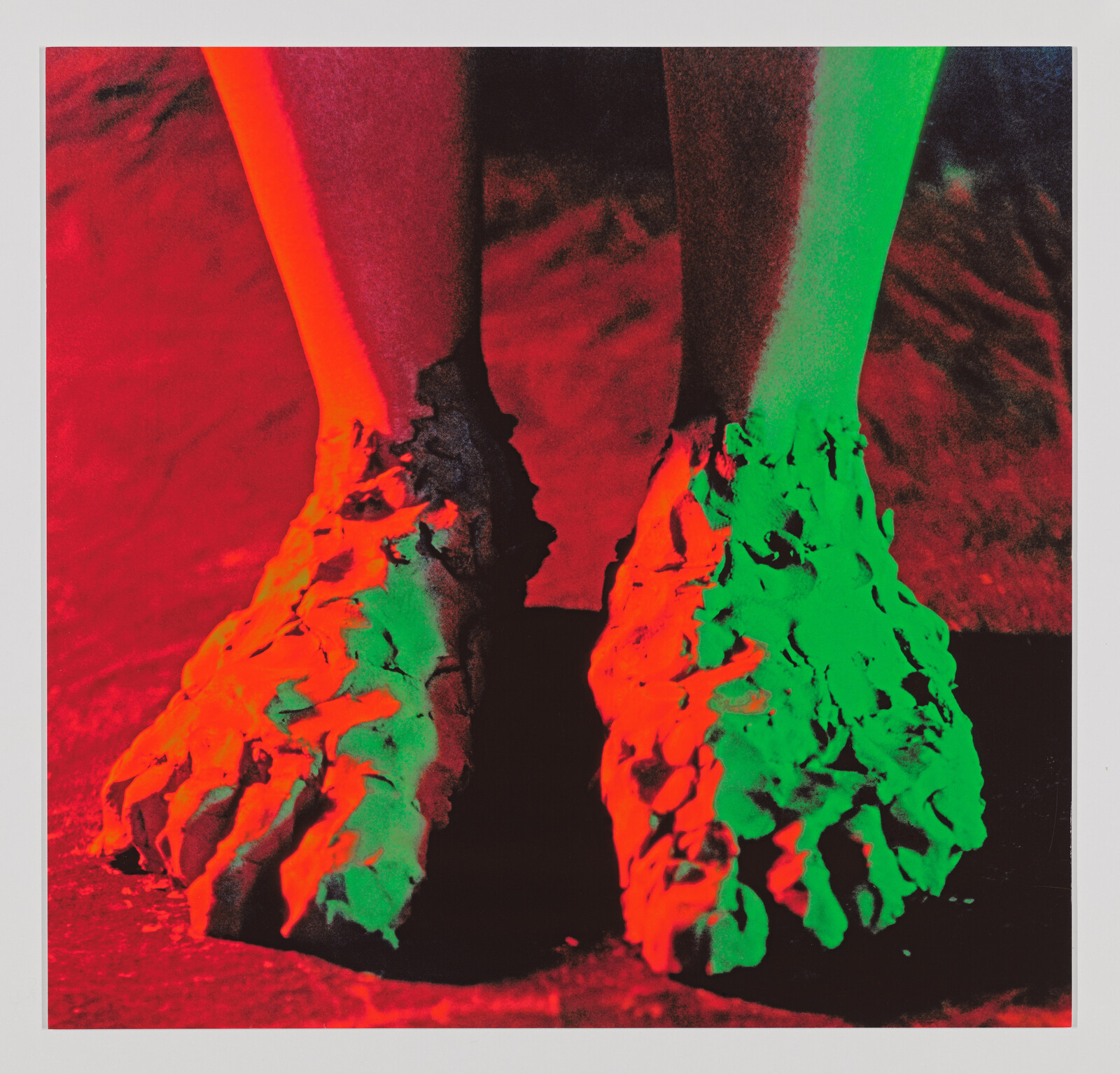 Two feet covered in thick clay-like mud under red and green colored lighting.