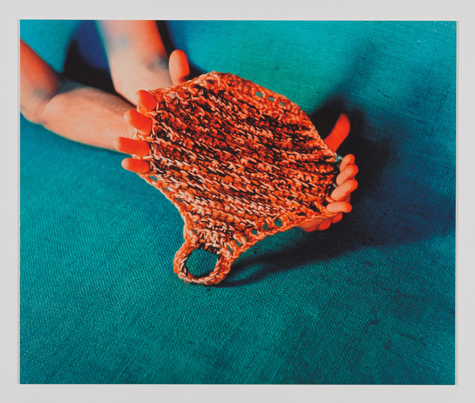 A person holds an orange knitted dishcloth with a small loop over a teal surface.