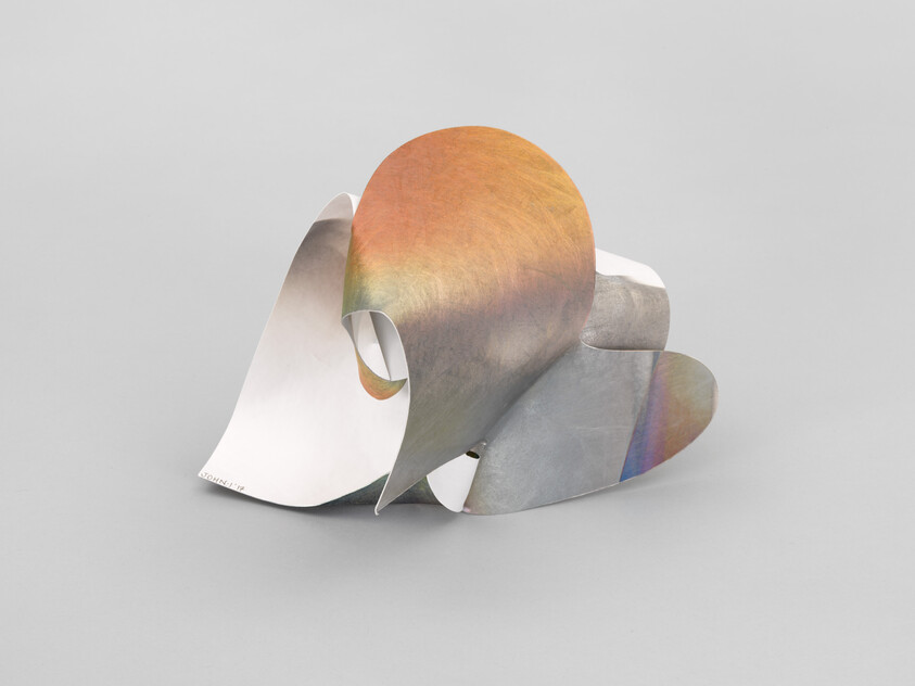 Curved iridescent metal sheets folded into an abstract, looped tabletop sculpture.