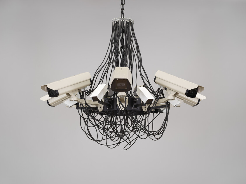 A chandelier-like cluster of surveillance cameras hangs from the ceiling with tangled black cables.