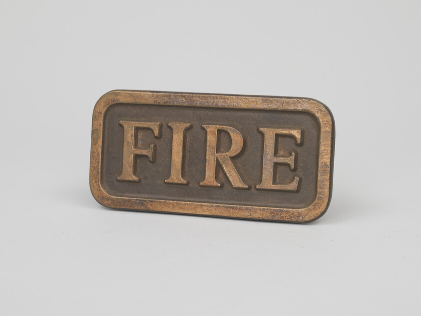 Bronze rectangular plaque engraved with the word FIRE placed against a light background.