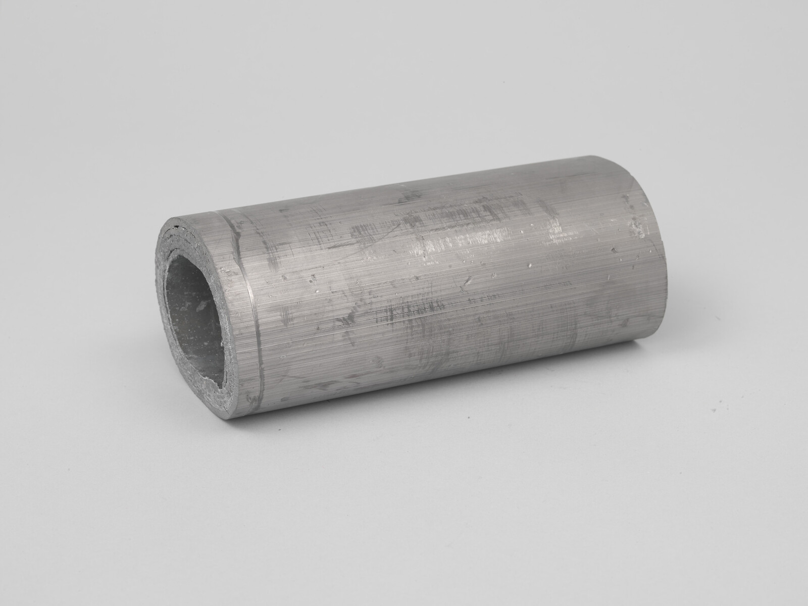 Hollow metal cylinder with rough inner edge resting on a flat surface.