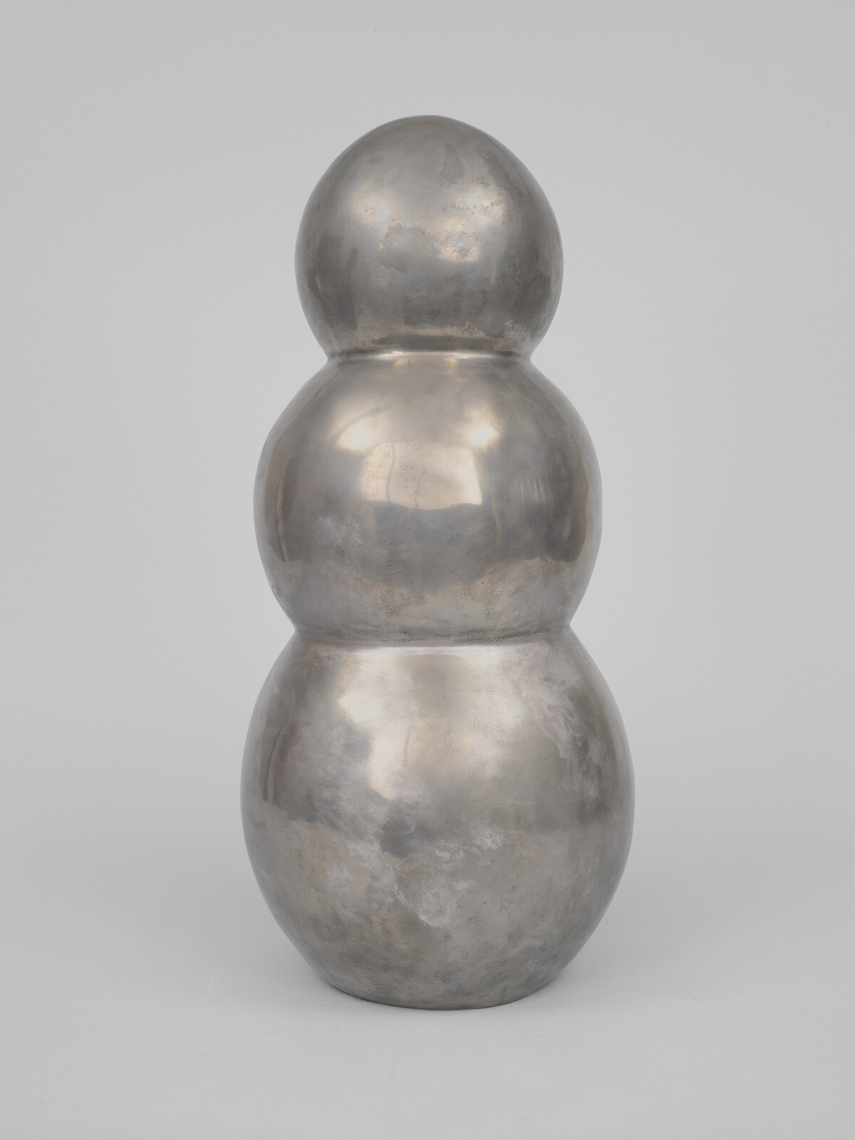 Polished metal sculpture made of three stacked bulbous forms with a smooth reflective surface.