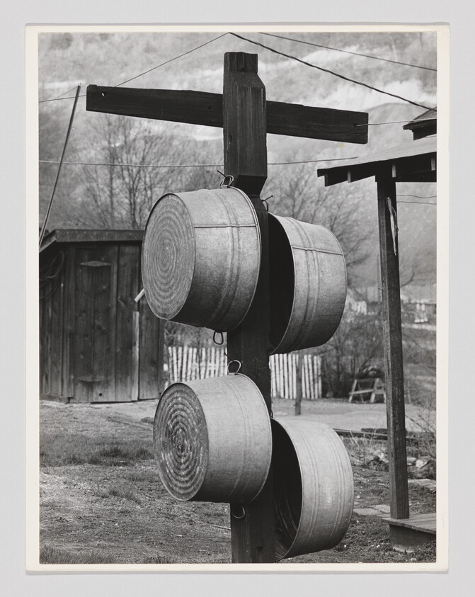 Four galvanized wash tubs hang from a wooden post in a yard near a shed and fence.
