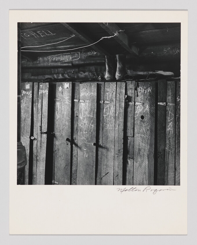 Worn wooden planks with chalk markings and a pair of boots resting on an overhead beam.