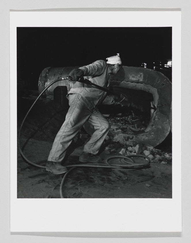 A worker uses a hose to clean the interior of a large metal pipe at night.