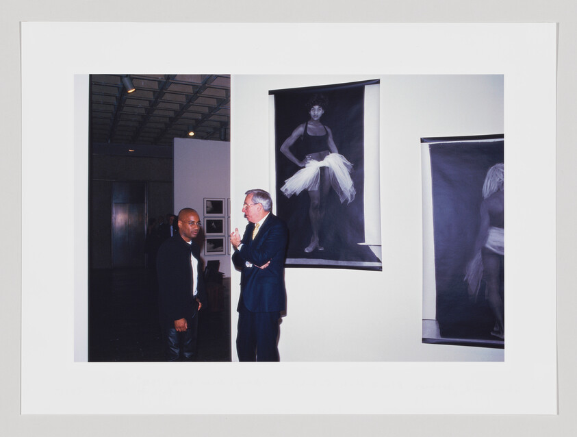 Two men engaged in conversation at an art gallery with large framed photographs of a dancer on the walls.