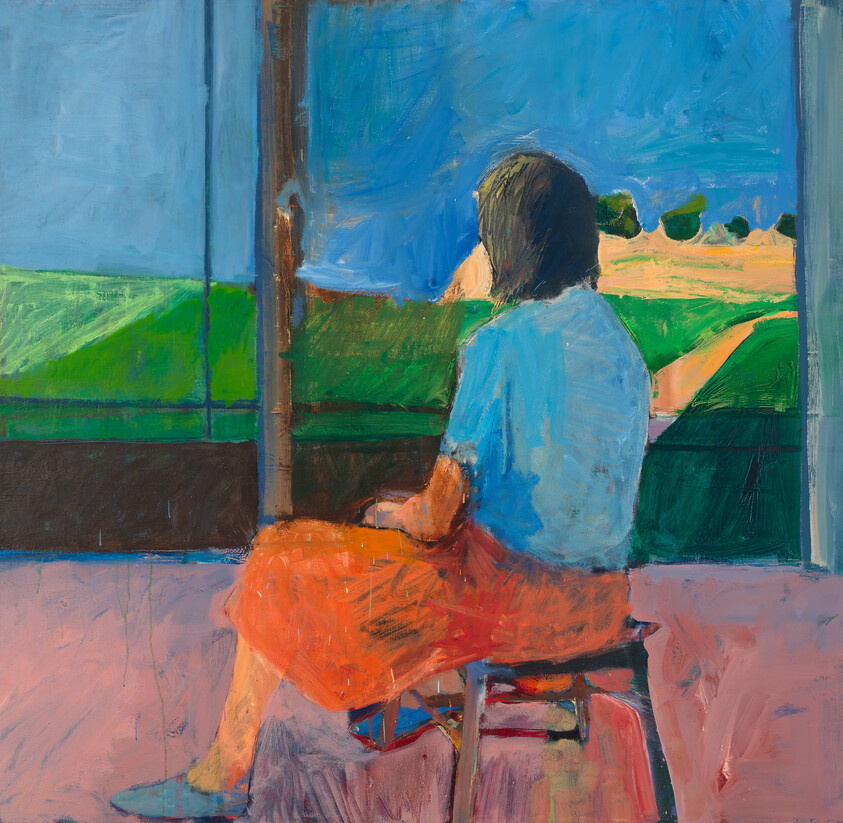 A woman in a blue shirt and orange skirt sits on a stool looking out at green fields.