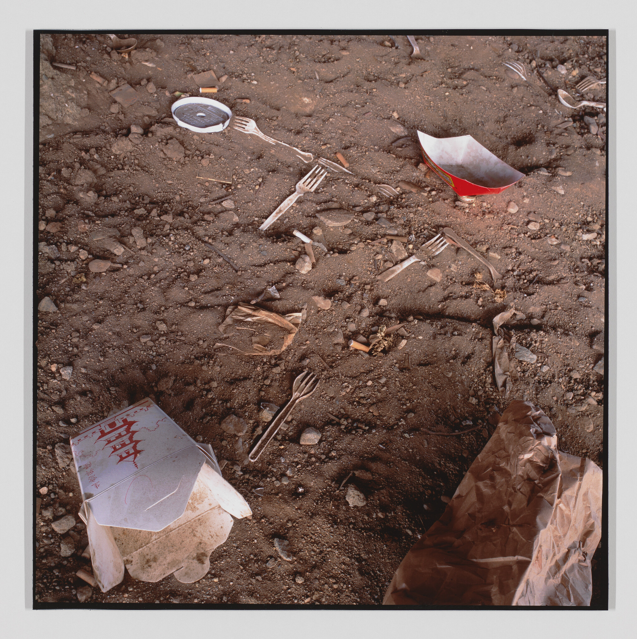 Discarded takeout boxes, plastic forks, and cigarette butts scattered across a dirt-covered ground.