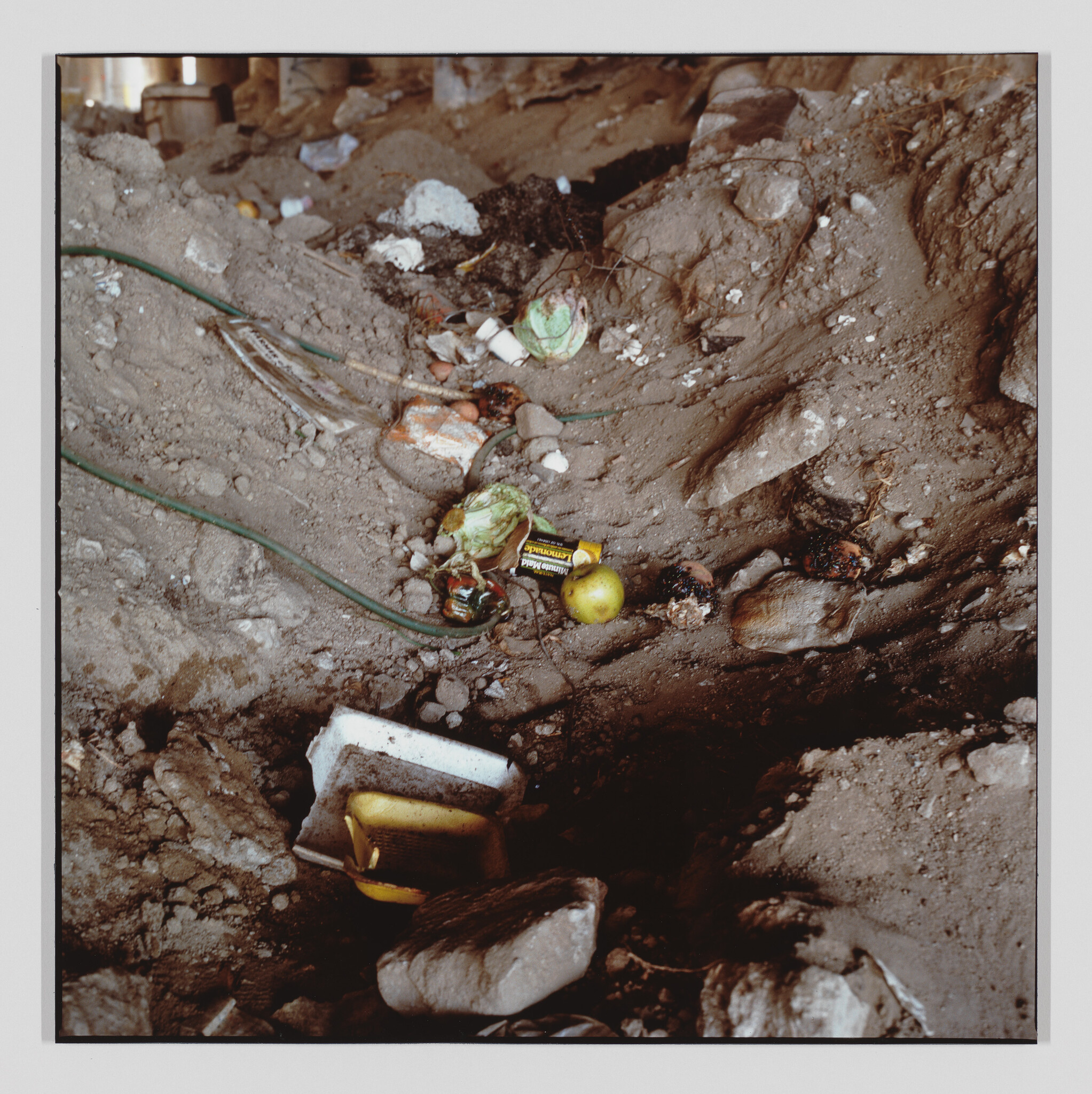 A muddy area littered with cables, batteries, rotting fruit, and broken foam pieces.