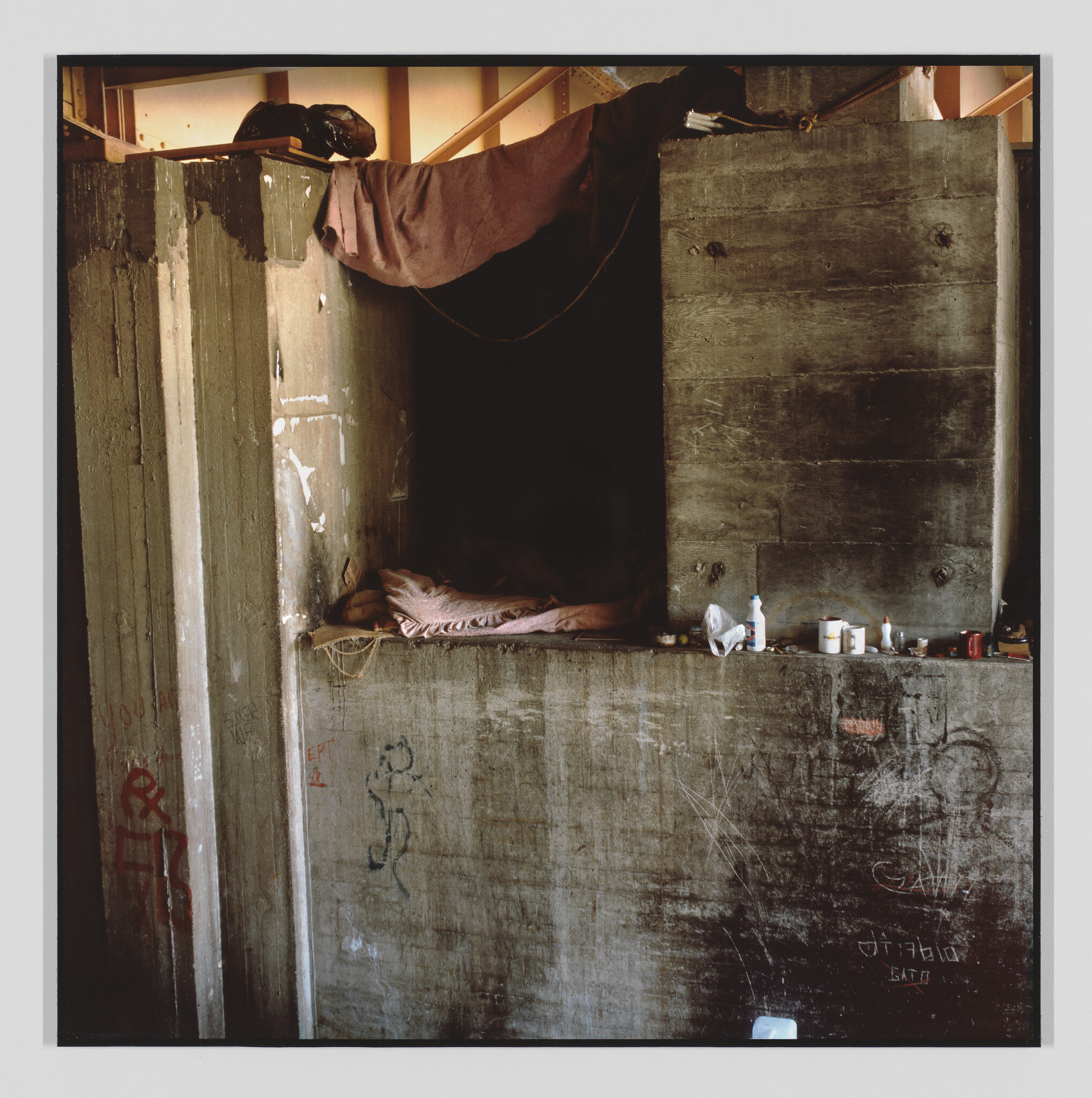 A makeshift sleeping nook with a blanket and personal items inside a concrete alcove.