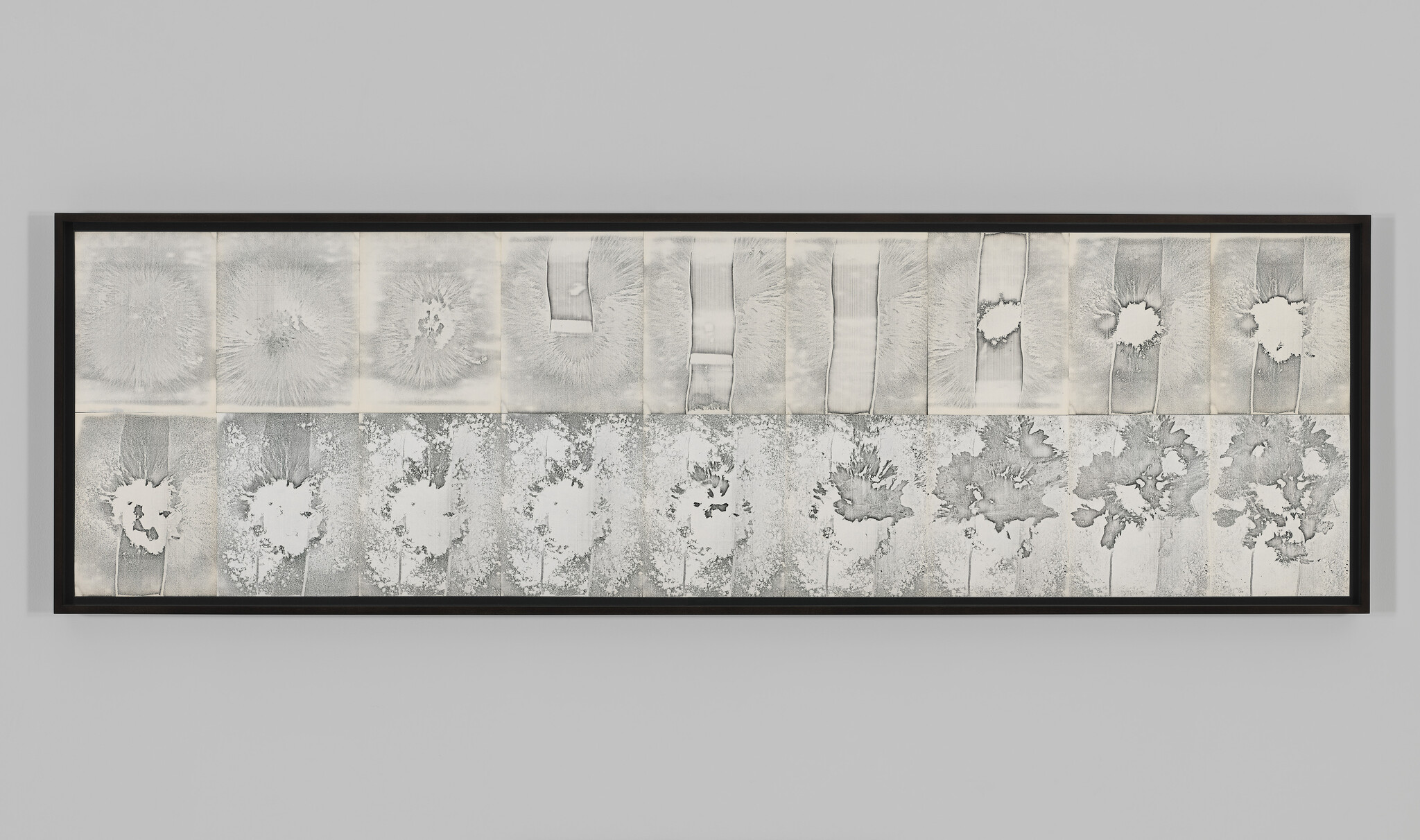 Long framed artwork showing two rows of monochrome textured prints with circular bursts and irregular splatters.