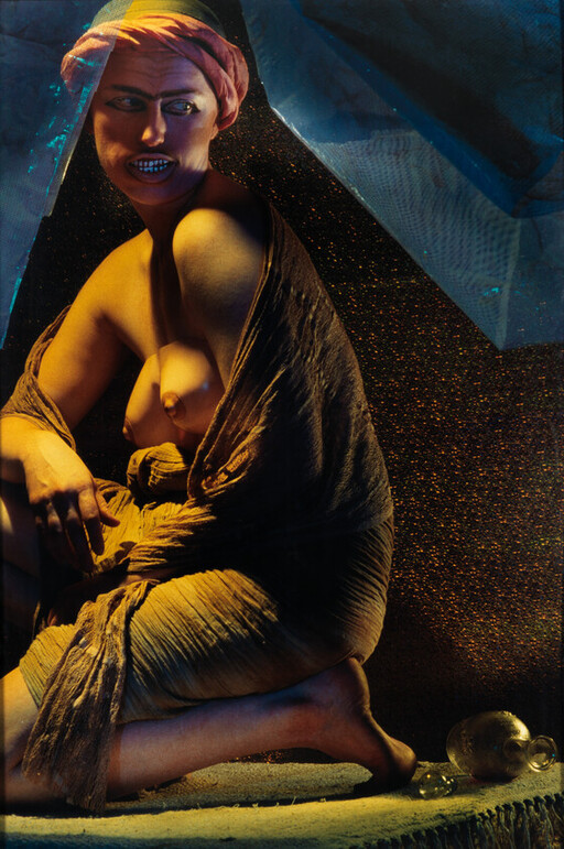 A crouching person wrapped in draped cloth and a headscarf under dramatic lighting.