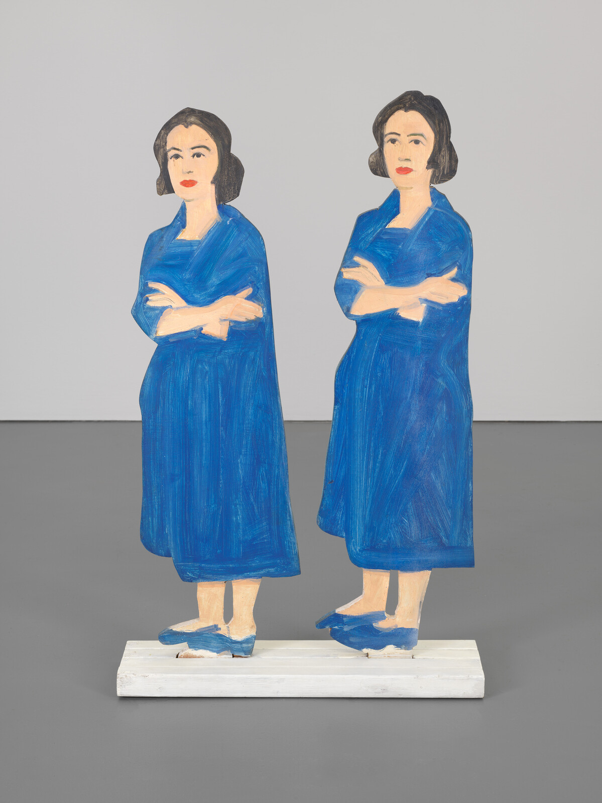 Two painted wooden cutouts of women in blue dresses standing side by side with arms crossed.