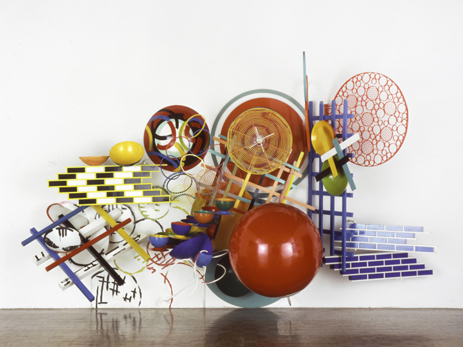 A large colorful three-dimensional wall sculpture composed of circles, grids, bowls, and ladders.