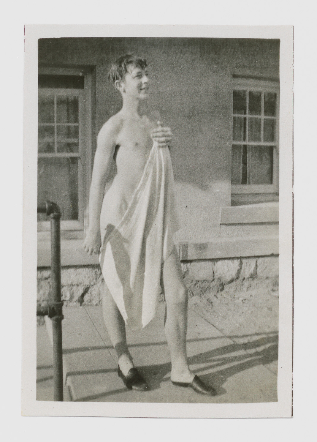 A person standing outdoors holding a towel to cover themselves while wearing shoes.