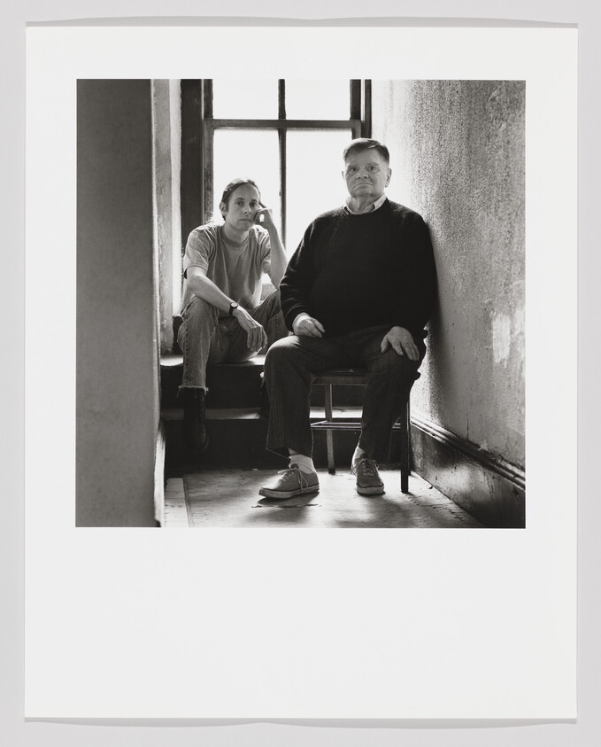 Two people sit quietly in a narrow, light-filled stairwell by a window.