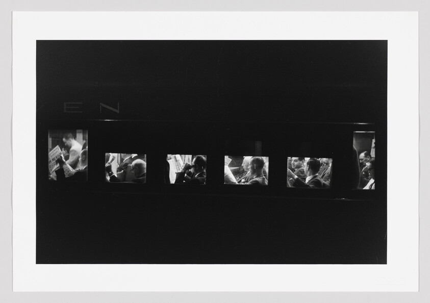 Commuters sit in a dark train car, each visible through small lit windows reading newspapers.