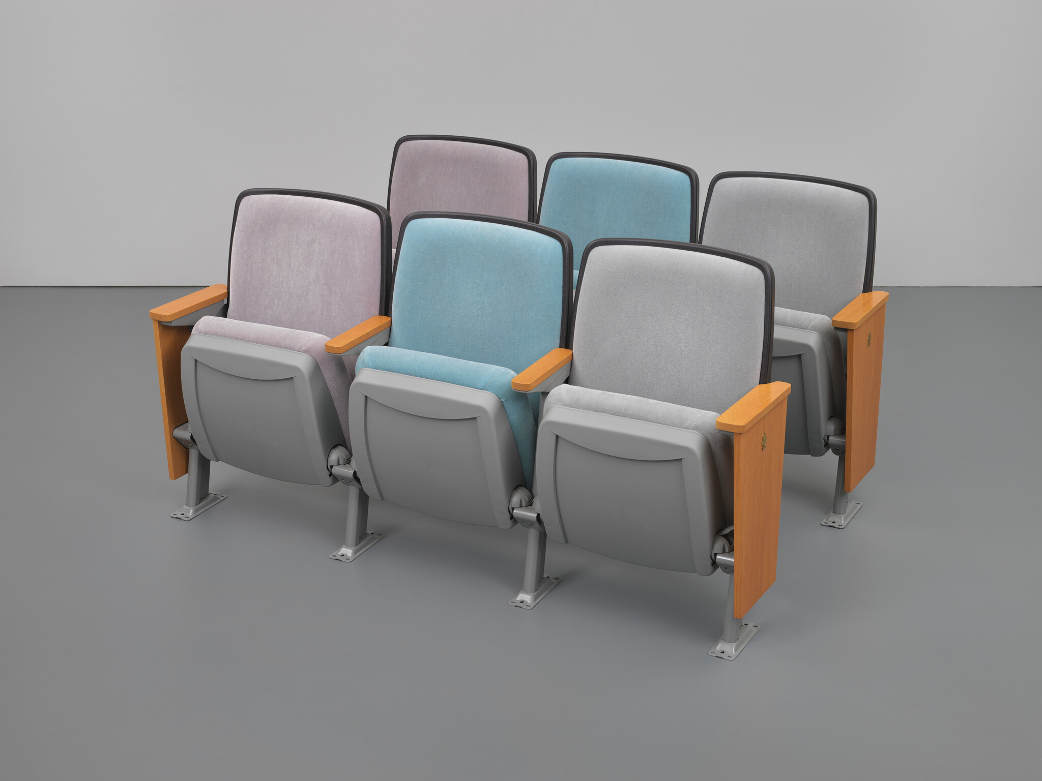 Six connected auditorium seats in pastel blue, gray, and pink with wooden armrests arranged in two rows.