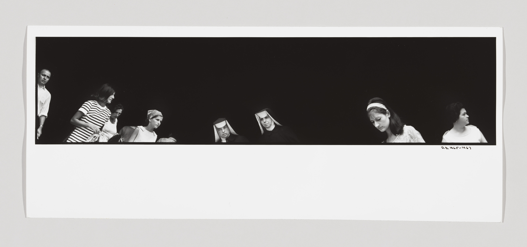 A panoramic black and white photograph featuring a series of individuals against a dark background, including two nuns in traditional habits, a woman in a striped dress, and others in various attire, all seemingly engaged in separate activities or thoughts.