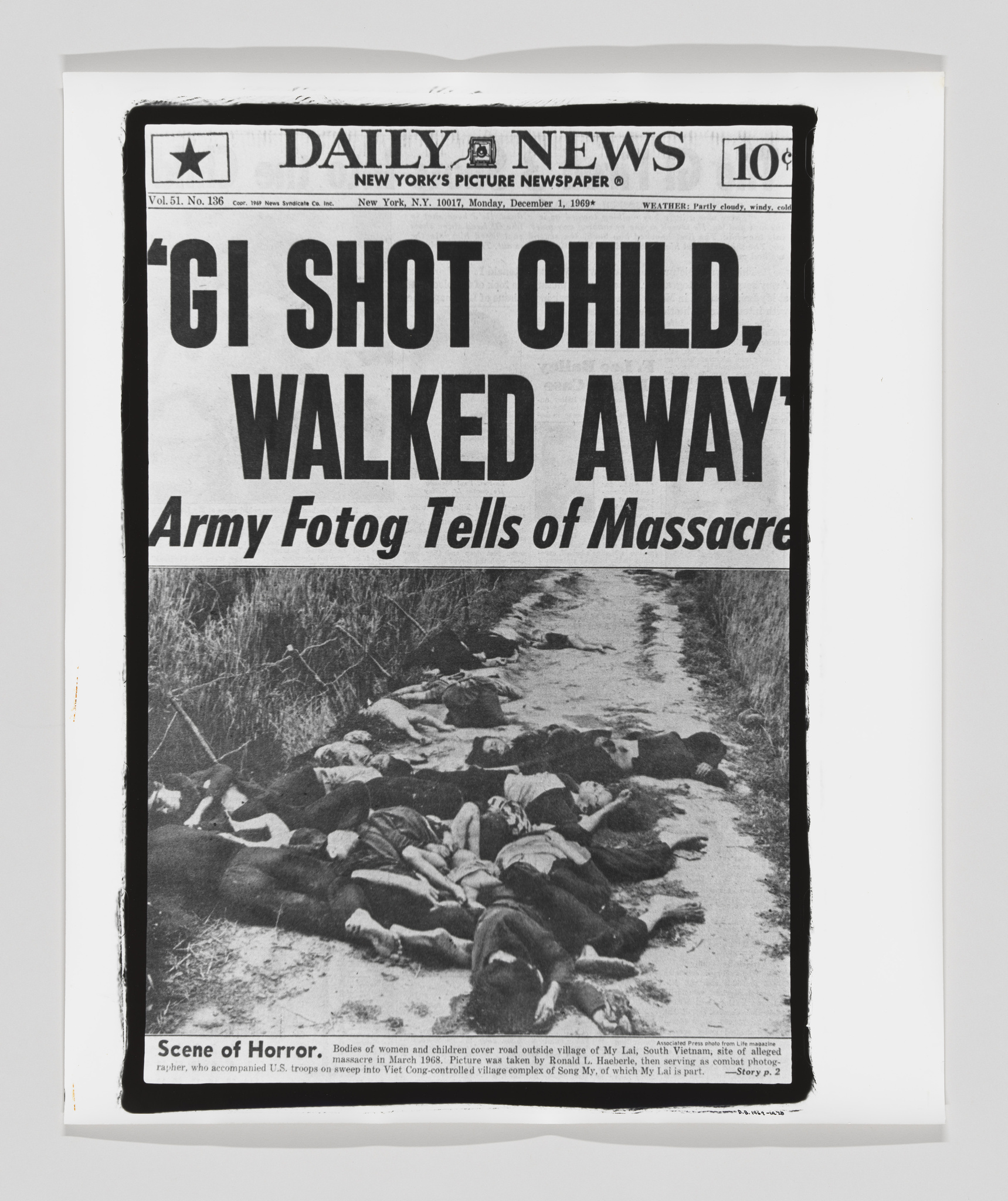 A black and white photograph of a historical newspaper, the Daily News, with a headline about a GI shooting a child and walking away, and a subheadline about an Army photographer telling of a massacre. The accompanying image shows bodies of women and children near a road, which is a scene from the My Lai massacre during the Vietnam War. The newspaper is slightly curled at the edges, indicating it may be an archived or preserved copy.