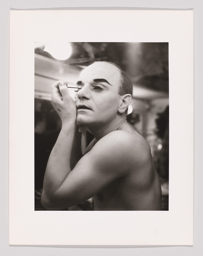 A person applies mascara at a backstage mirror, preparing for a performance.