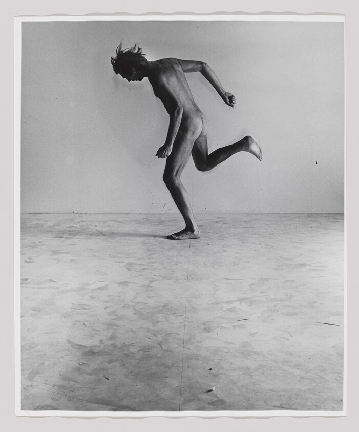A nude person balances on one foot while leaning forward with the other leg lifted behind.