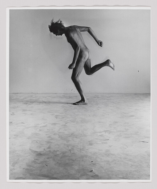 A nude person captured mid-stride, balancing on one foot with the other leg bent behind.