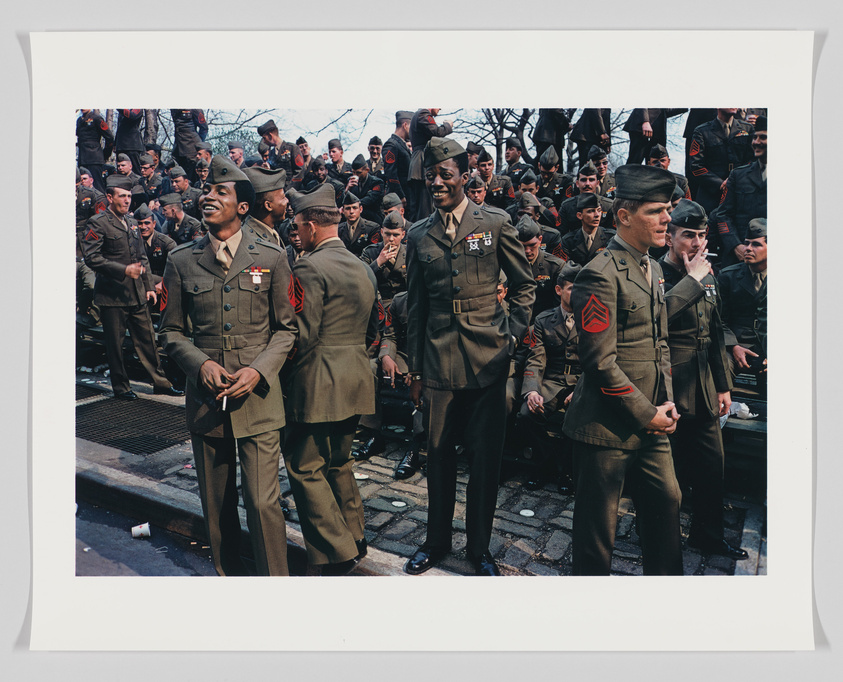 A group of military personnel in uniform, with some smiling and chatting, gathered in an outdoor setting, possibly during a public event or ceremony.