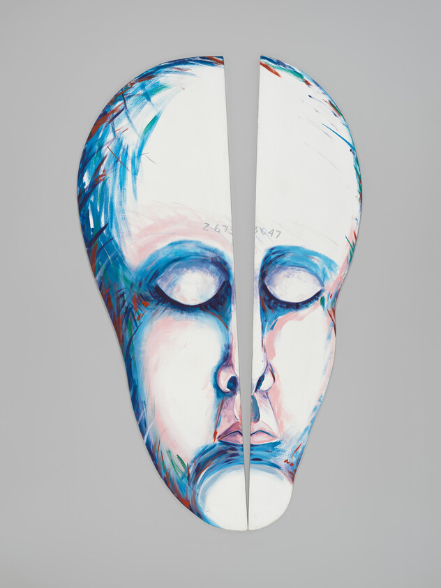 Large painted face mask split down the middle showing closed eyes and soft blue-pink strokes.