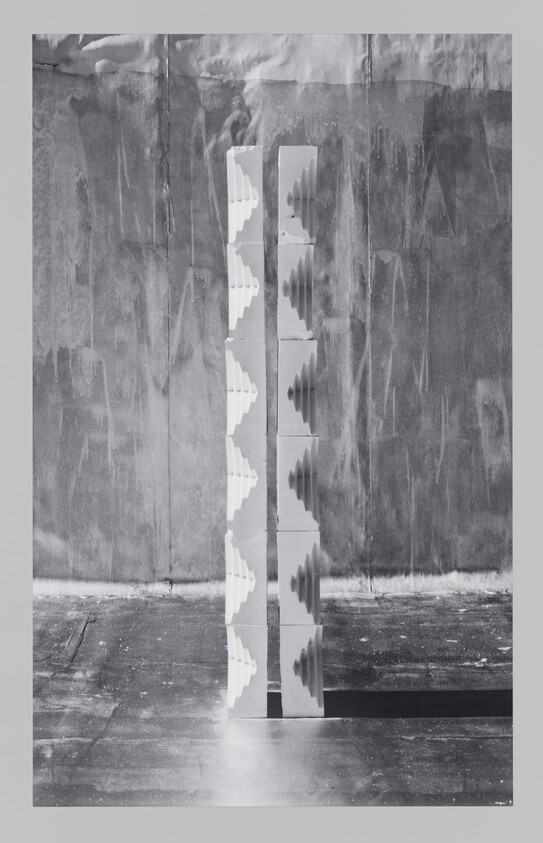 Two tall white stacked columns with stepped cutouts stand side by side casting a long shadow.