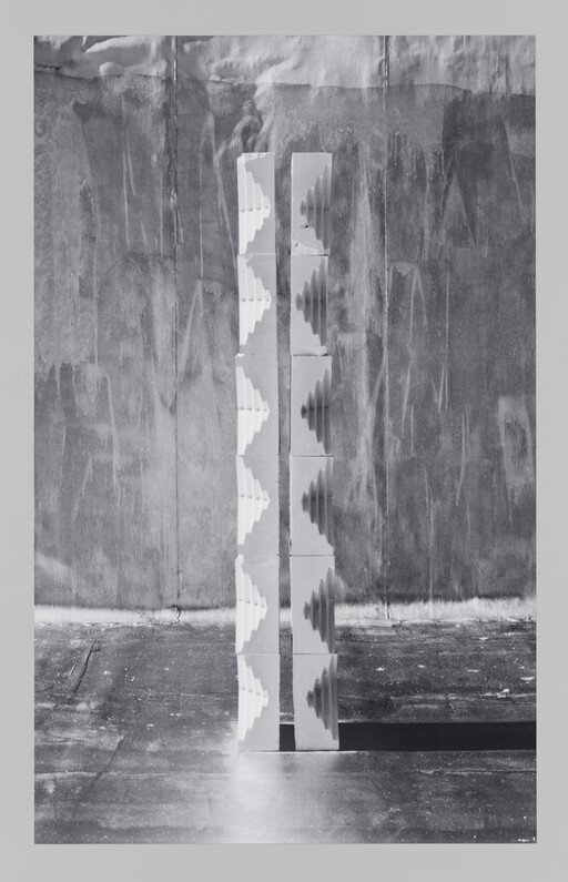 Two tall white stacked columns with stepped cutouts stand side by side casting a long shadow.